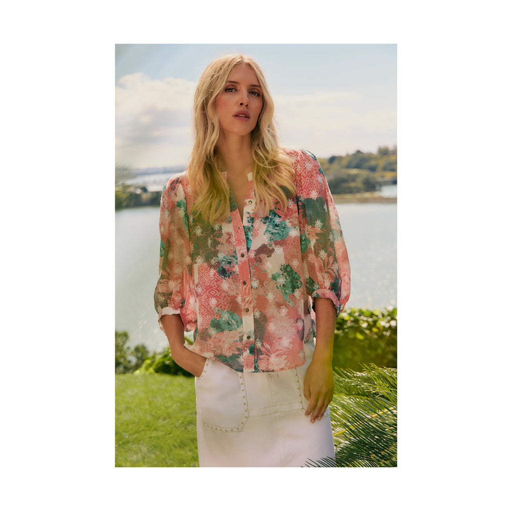 Woman wearing a floral blouse standing outdoors with a scenic background