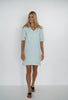 A light blue Promise dress, worn by a lady with hands on her side, front view